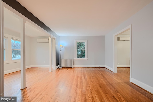 interior space featuring baseboards, a wall unit AC, radiator heating unit, and light wood-style floors