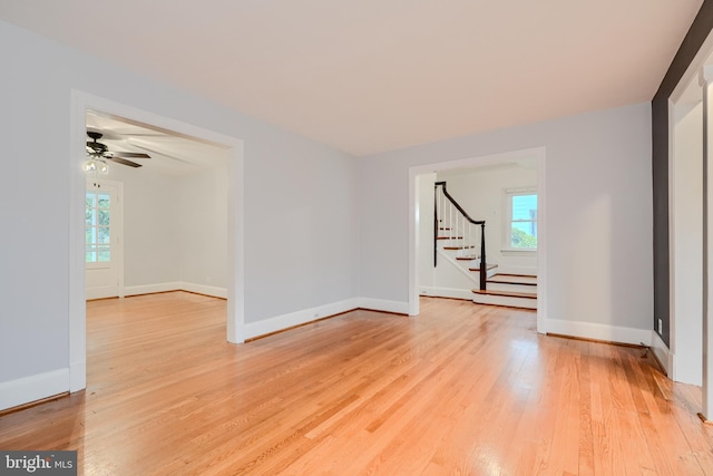 unfurnished room featuring baseboards, a ceiling fan, light wood-type flooring, and stairs