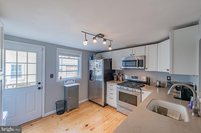 kitchen with light countertops, stainless steel appliances, a sink, light wood finished floors, and white cabinets