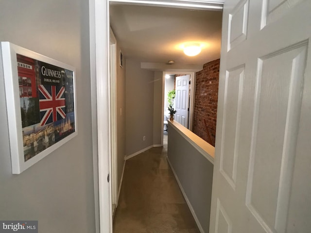 hallway featuring dark colored carpet, brick wall, baseboards, and visible vents
