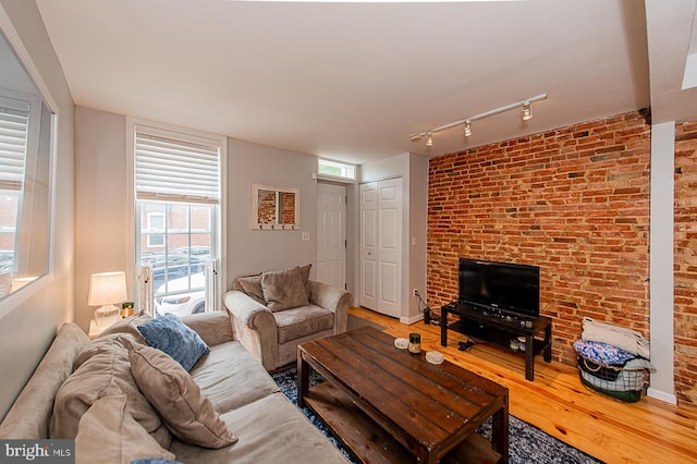 living room featuring baseboards, wood finished floors, rail lighting, and brick wall