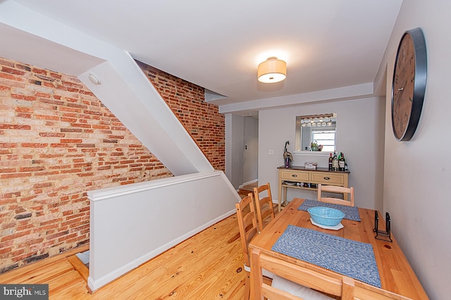 dining space with baseboards, wood finished floors, and brick wall