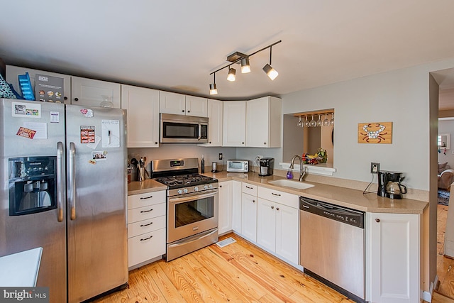 kitchen featuring white cabinetry, light countertops, stainless steel appliances, a sink, and light wood-style floors