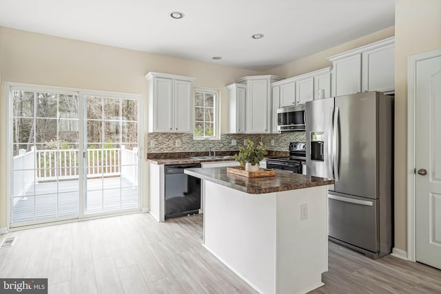 kitchen with tasteful backsplash, light wood-type flooring, dark countertops, a kitchen island, and appliances with stainless steel finishes