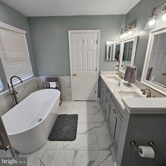 bathroom with a sink, a wainscoted wall, marble finish floor, and a freestanding tub