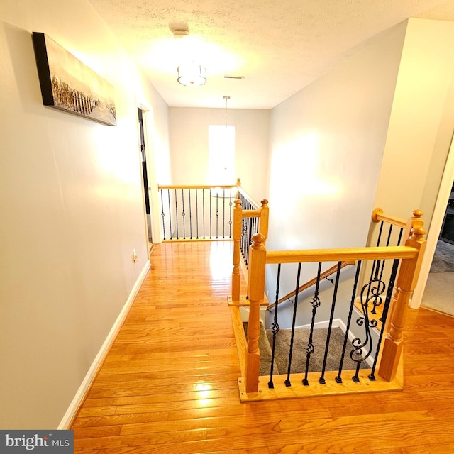 hallway featuring baseboards, visible vents, wood-type flooring, and an upstairs landing