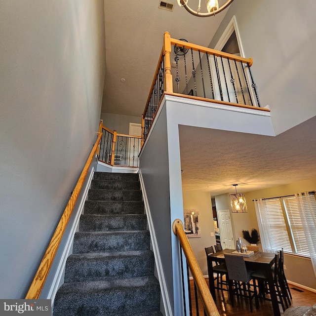 stairway featuring baseboards, an inviting chandelier, a high ceiling, visible vents, and wood finished floors