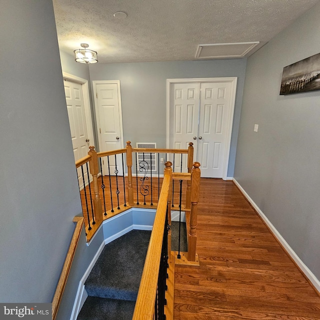 staircase with a textured ceiling, wood finished floors, attic access, and baseboards