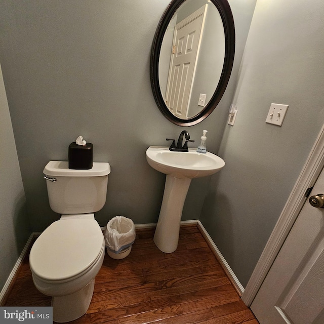 half bathroom featuring toilet, wood finished floors, a sink, and baseboards