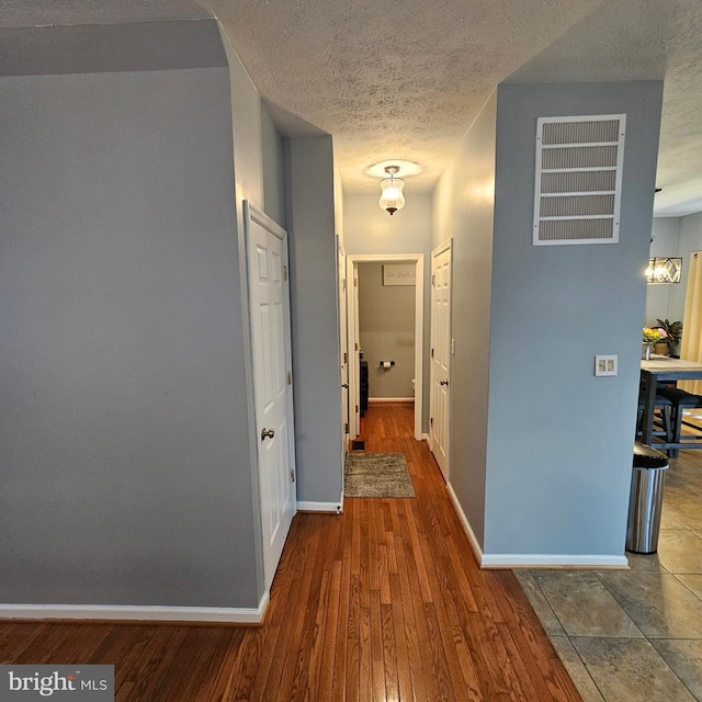 hallway featuring visible vents, baseboards, wood finished floors, and a textured ceiling