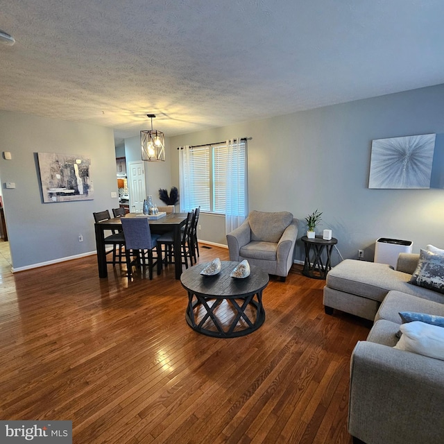 living room featuring a chandelier, a textured ceiling, wood-type flooring, and baseboards