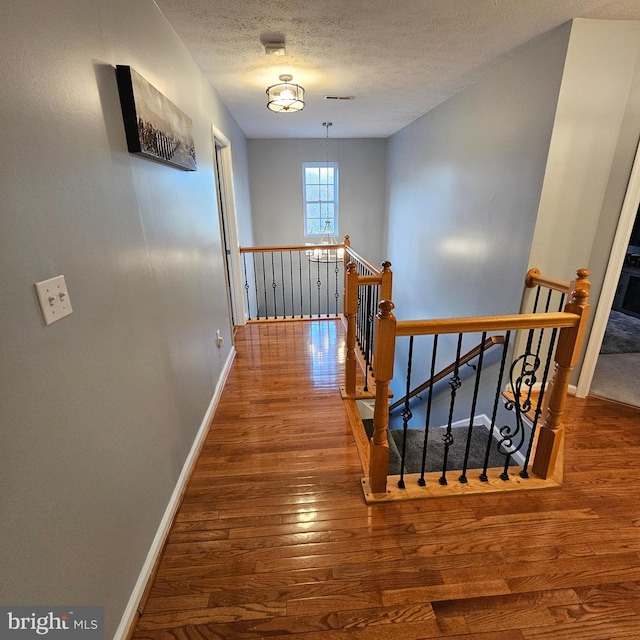 hallway with visible vents, baseboards, an upstairs landing, a textured ceiling, and wood-type flooring