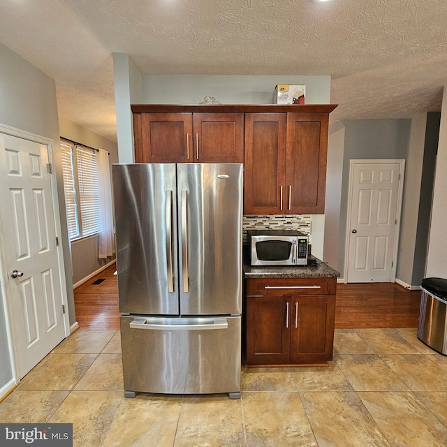 kitchen featuring a textured ceiling, decorative backsplash, baseboards, and stainless steel appliances