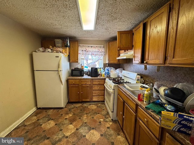 kitchen featuring under cabinet range hood, a sink, brown cabinetry, and white appliances