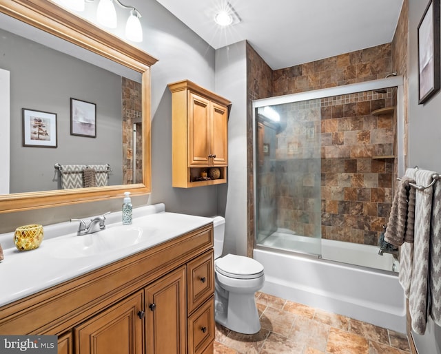 bathroom with combined bath / shower with glass door, vanity, stone finish flooring, and toilet