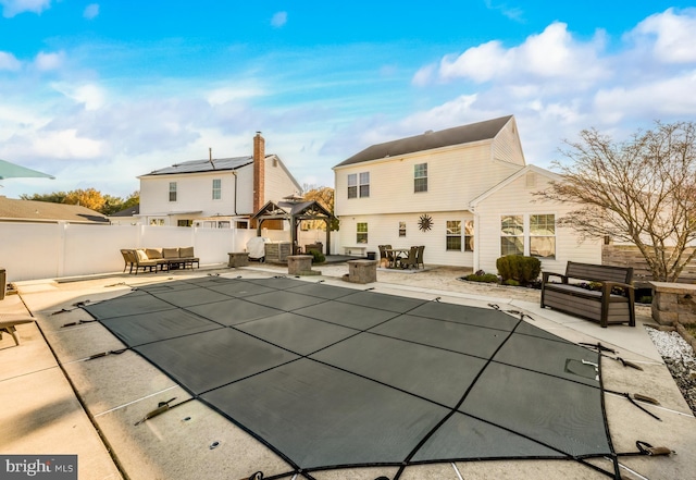 rear view of property featuring a fire pit, a patio area, a gazebo, a fenced backyard, and a fenced in pool