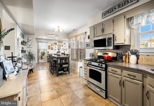 kitchen featuring baseboards, light tile patterned floors, dark countertops, decorative backsplash, and stainless steel appliances
