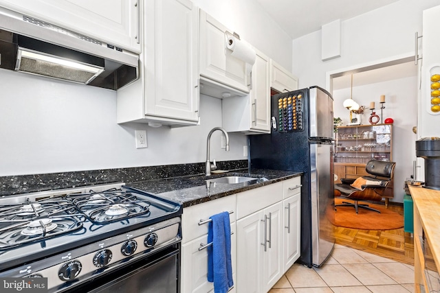 kitchen featuring white cabinetry, dark stone countertops, a sink, gas range oven, and extractor fan