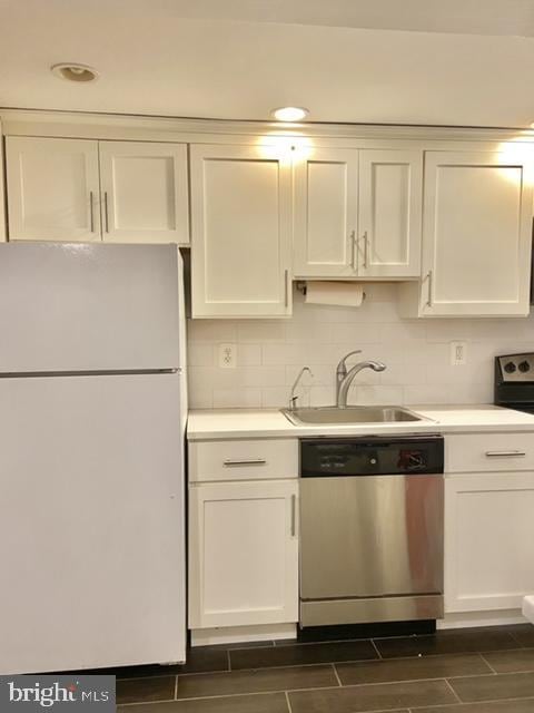 kitchen with light countertops, white cabinetry, a sink, stainless steel dishwasher, and freestanding refrigerator