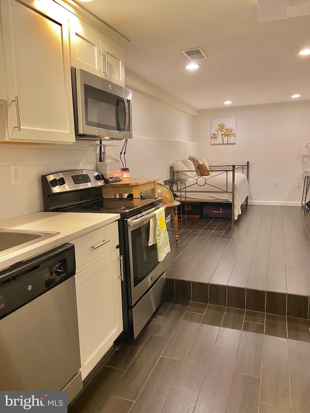 kitchen featuring wood tiled floor, white cabinetry, tasteful backsplash, and appliances with stainless steel finishes
