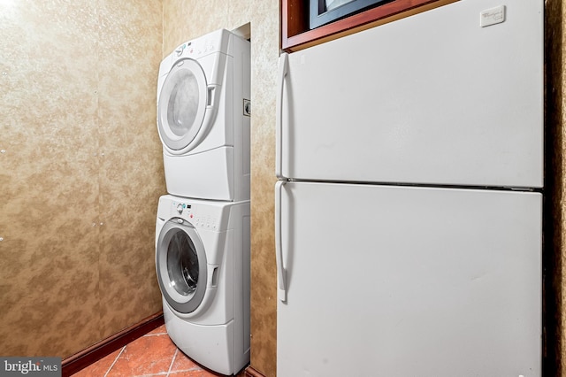 clothes washing area featuring tile patterned flooring, baseboards, stacked washer / dryer, and laundry area