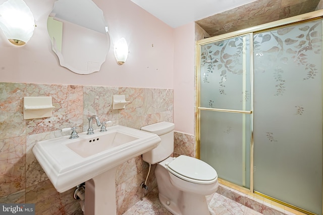 full bath featuring a wainscoted wall, toilet, a sink, tile walls, and a stall shower