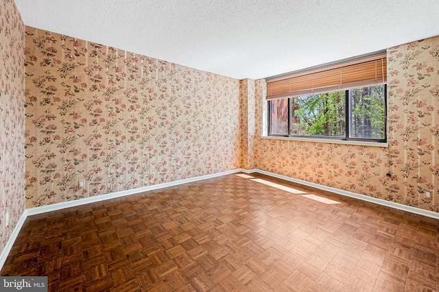 empty room with baseboards, a textured ceiling, and wallpapered walls