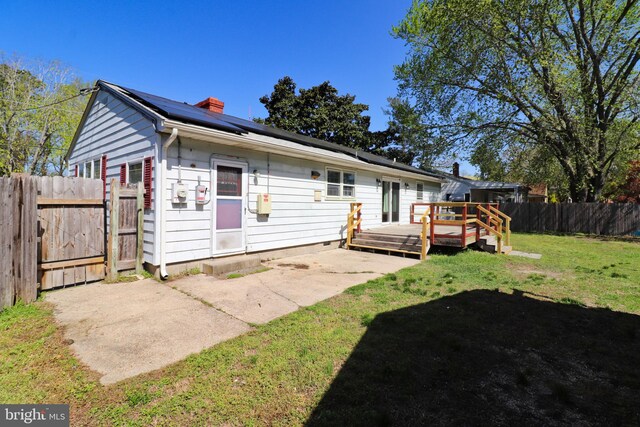 1405 Westchester St, Salisbury, MD 21801 - back of house with a chimney, a fenced backyard, a wooden deck, solar panels, and a lawn