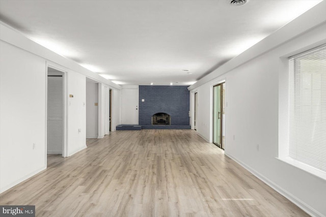 unfurnished living room with a brick fireplace, light wood finished floors, and baseboards