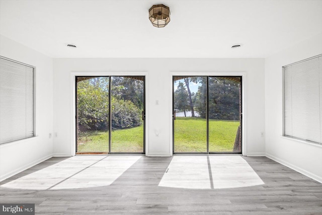 unfurnished living room featuring healthy amount of natural light, wood finished floors, and baseboards