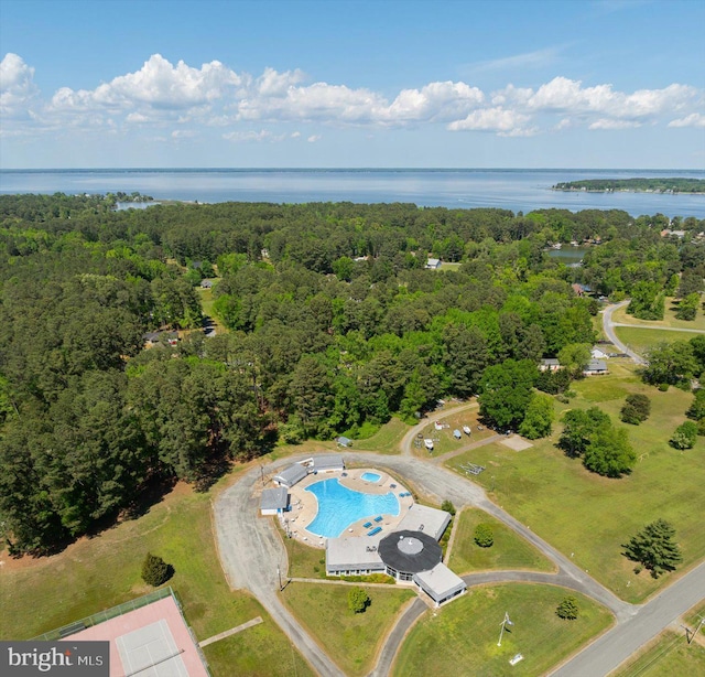 aerial view of property and surrounding area featuring a heavily wooded area, a large body of water, and a pool area