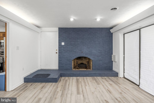 unfurnished living room featuring wood finished floors, a fireplace, baseboards, and brick wall