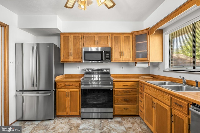 kitchen with appliances with stainless steel finishes, a sink, brown cabinetry, and glass insert cabinets