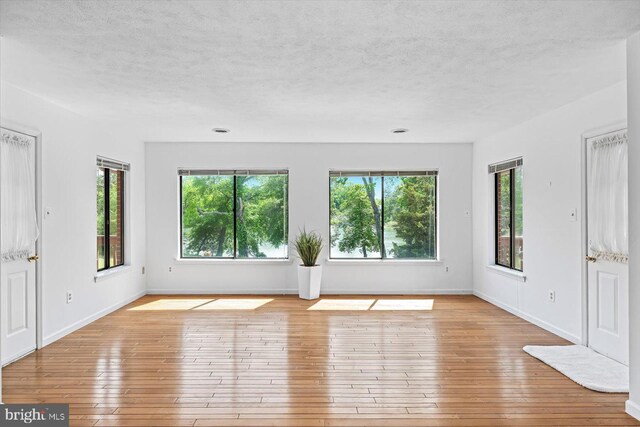 unfurnished living room with healthy amount of natural light, a textured ceiling, baseboards, and hardwood / wood-style floors