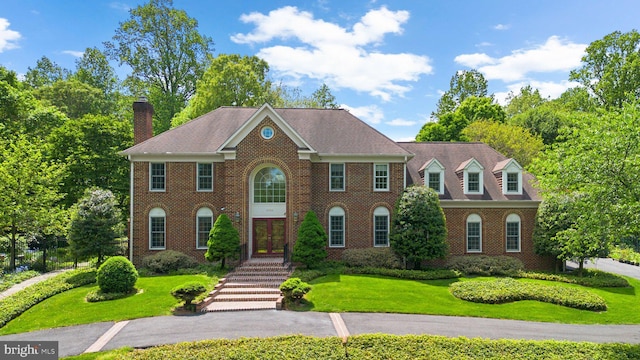 colonial home featuring french doors, a chimney, a front yard, and brick siding