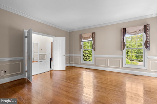 empty room featuring visible vents, crown molding, wood finished floors, a wainscoted wall, and a decorative wall