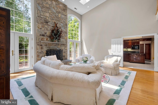 living room with light wood-type flooring, a fireplace, a skylight, and high vaulted ceiling