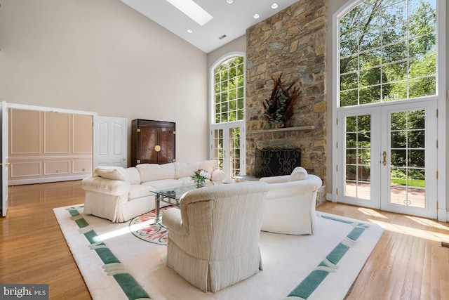 living room featuring high vaulted ceiling, a skylight, french doors, and wood finished floors