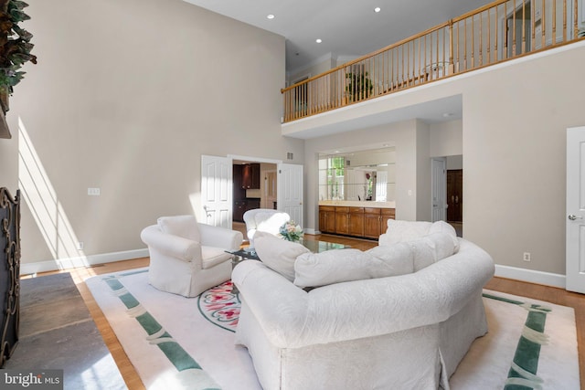 living area with baseboards, recessed lighting, light wood-style flooring, and a high ceiling
