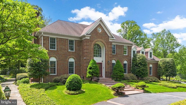 colonial-style house featuring fence, a shingled roof, a front lawn, and brick siding