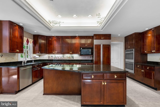 kitchen featuring appliances with stainless steel finishes, a center island, a sink, a raised ceiling, and dark stone counters