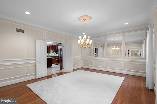 unfurnished dining area with an inviting chandelier, ornamental molding, visible vents, a decorative wall, and wood finished floors