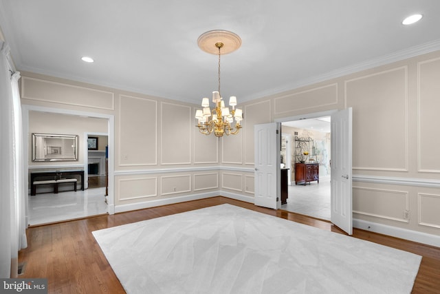 unfurnished dining area with dark wood-style floors, a notable chandelier, ornamental molding, and a decorative wall