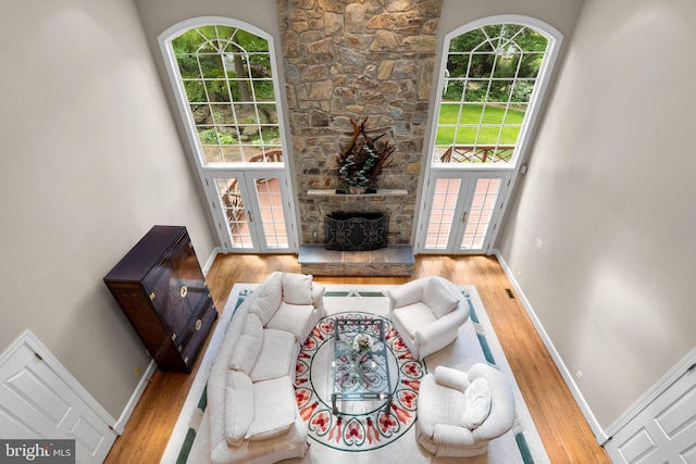 living area featuring baseboards, a stone fireplace, french doors, and wood finished floors