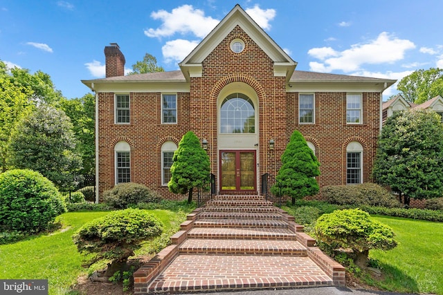 colonial home featuring brick siding, a front yard, french doors, and a chimney
