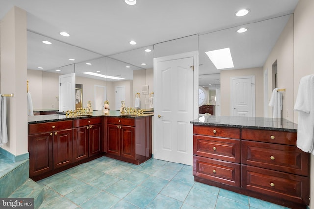 bathroom featuring tile patterned flooring, recessed lighting, a skylight, and vanity
