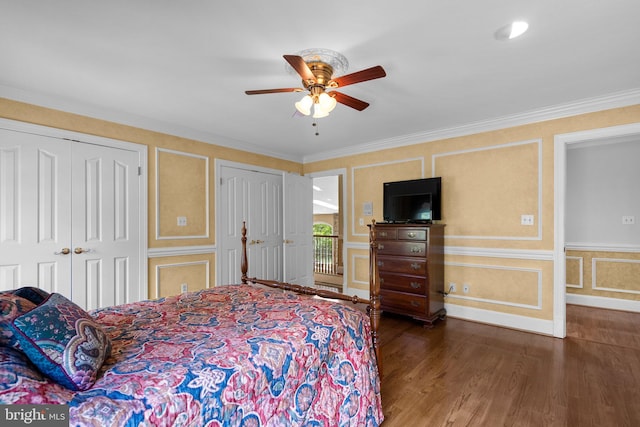 bedroom with ceiling fan, a decorative wall, multiple closets, wood finished floors, and ornamental molding