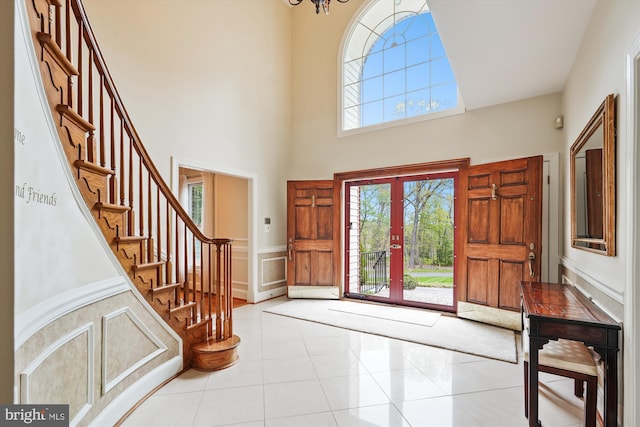 entryway with tile patterned flooring, a towering ceiling, a decorative wall, stairway, and a wainscoted wall