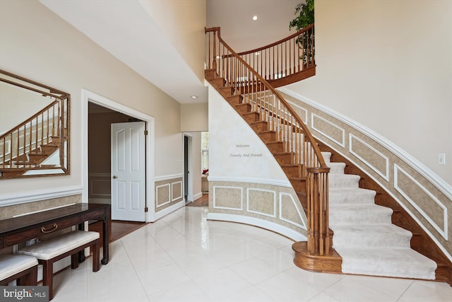 staircase with a decorative wall, wainscoting, tile patterned flooring, and a towering ceiling