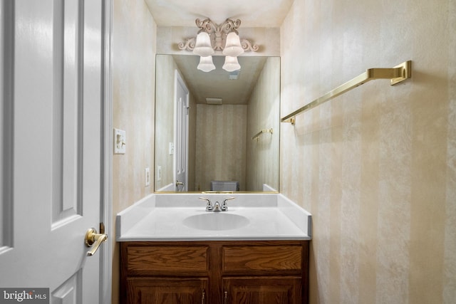 bathroom featuring an inviting chandelier, vanity, and wallpapered walls